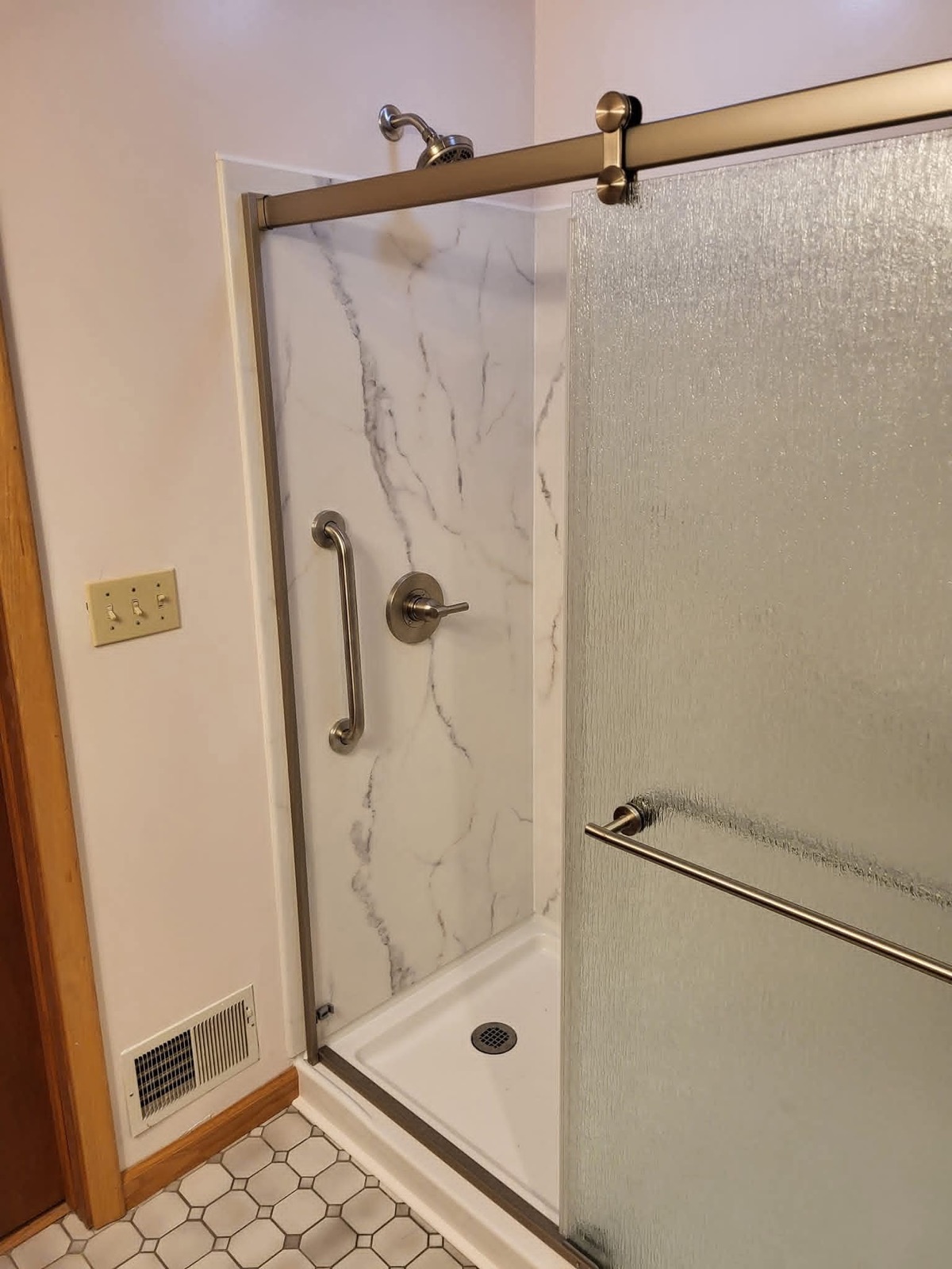 Finished bathroom shower with marble-look wall panels and a sliding textured-glass enclosure